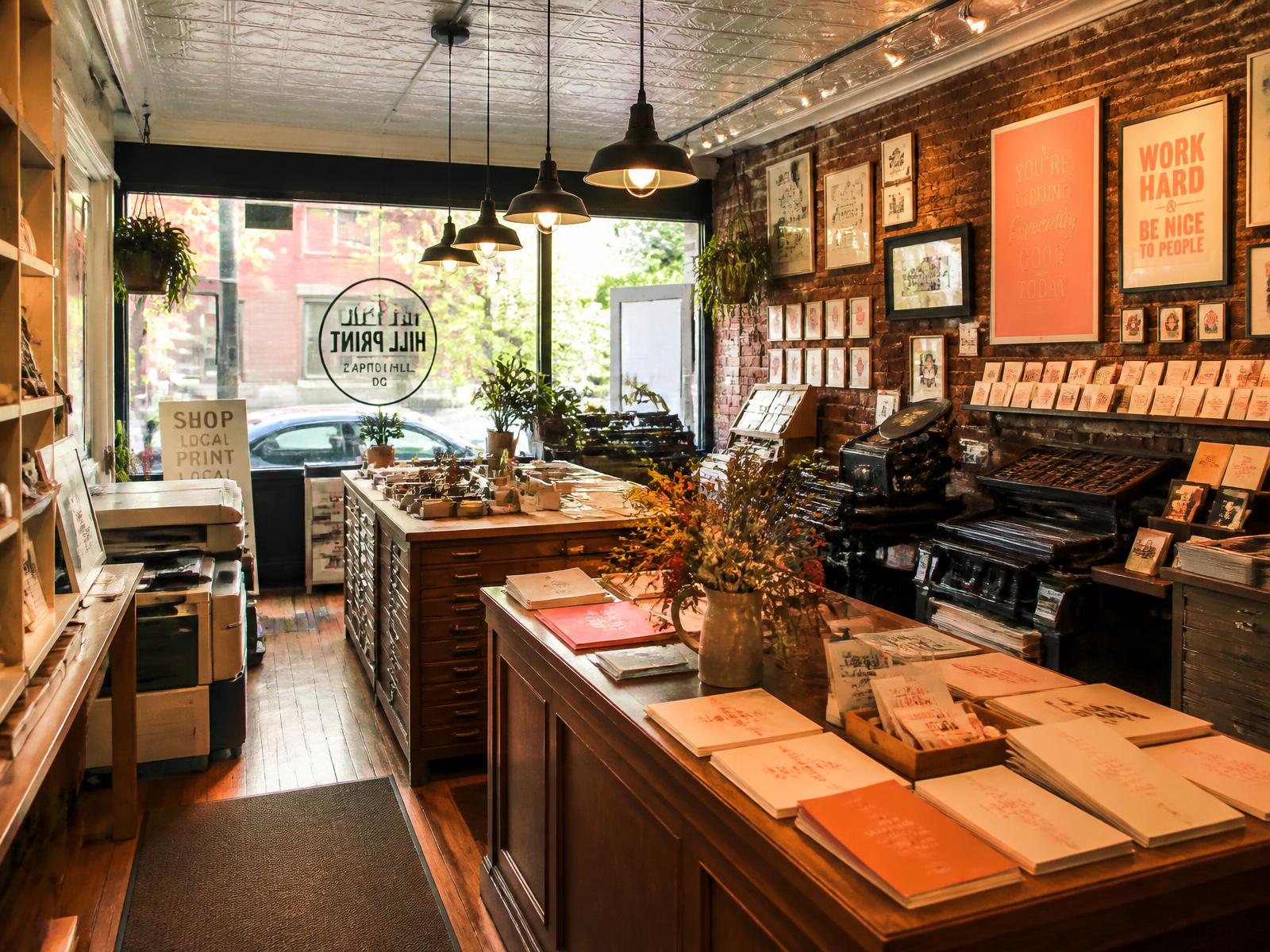 Interior of a small independent print shop with warm afternoon light, wooden counter, and walls of framed sample prints.