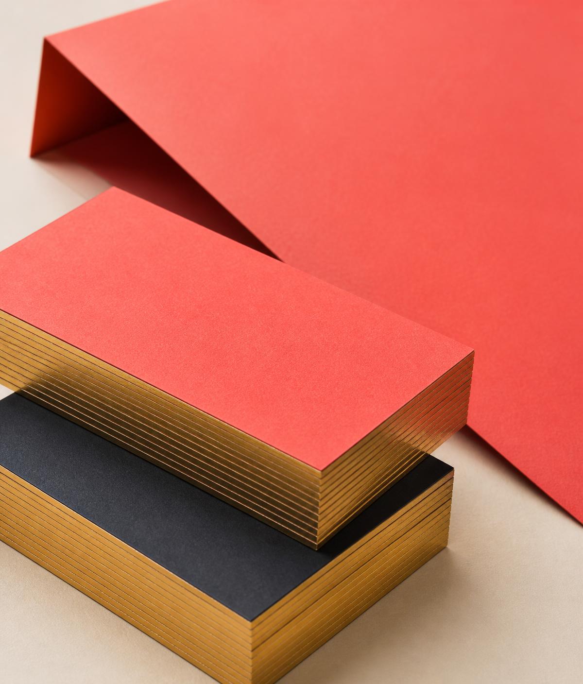 Stack of premium blank business cards with gold-foil painted edges in saturated coral and deep charcoal on a cream desk.